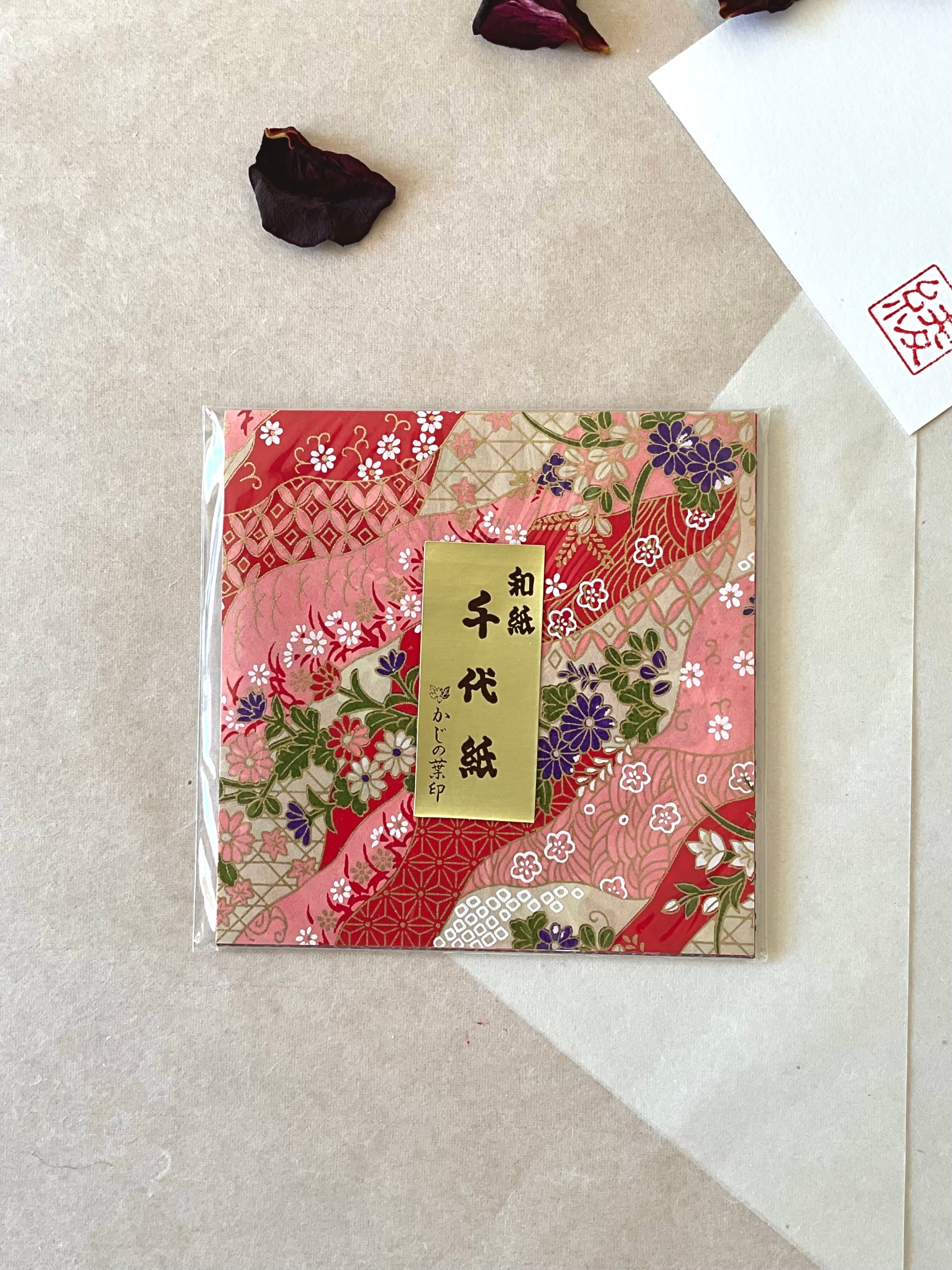 Single sealed pack of Morita Washi chiyogami origami paper with flowing pink and red wave pattern featuring wisteria, chrysanthemum and geometric panels in purple and gold, gold label