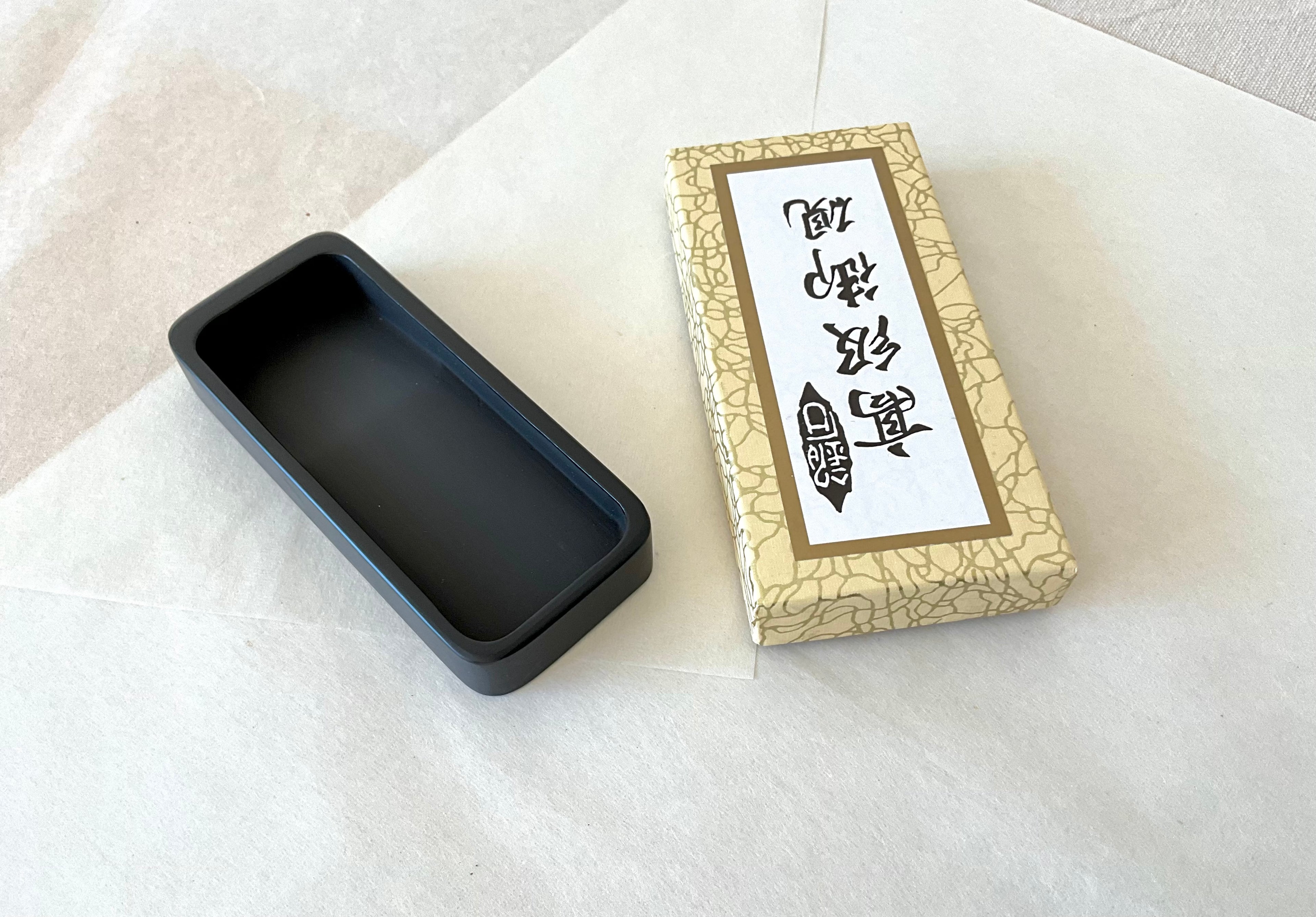 Traditional Japanese suzuri ink grinding stone with deep well beside gold box on layered paper
