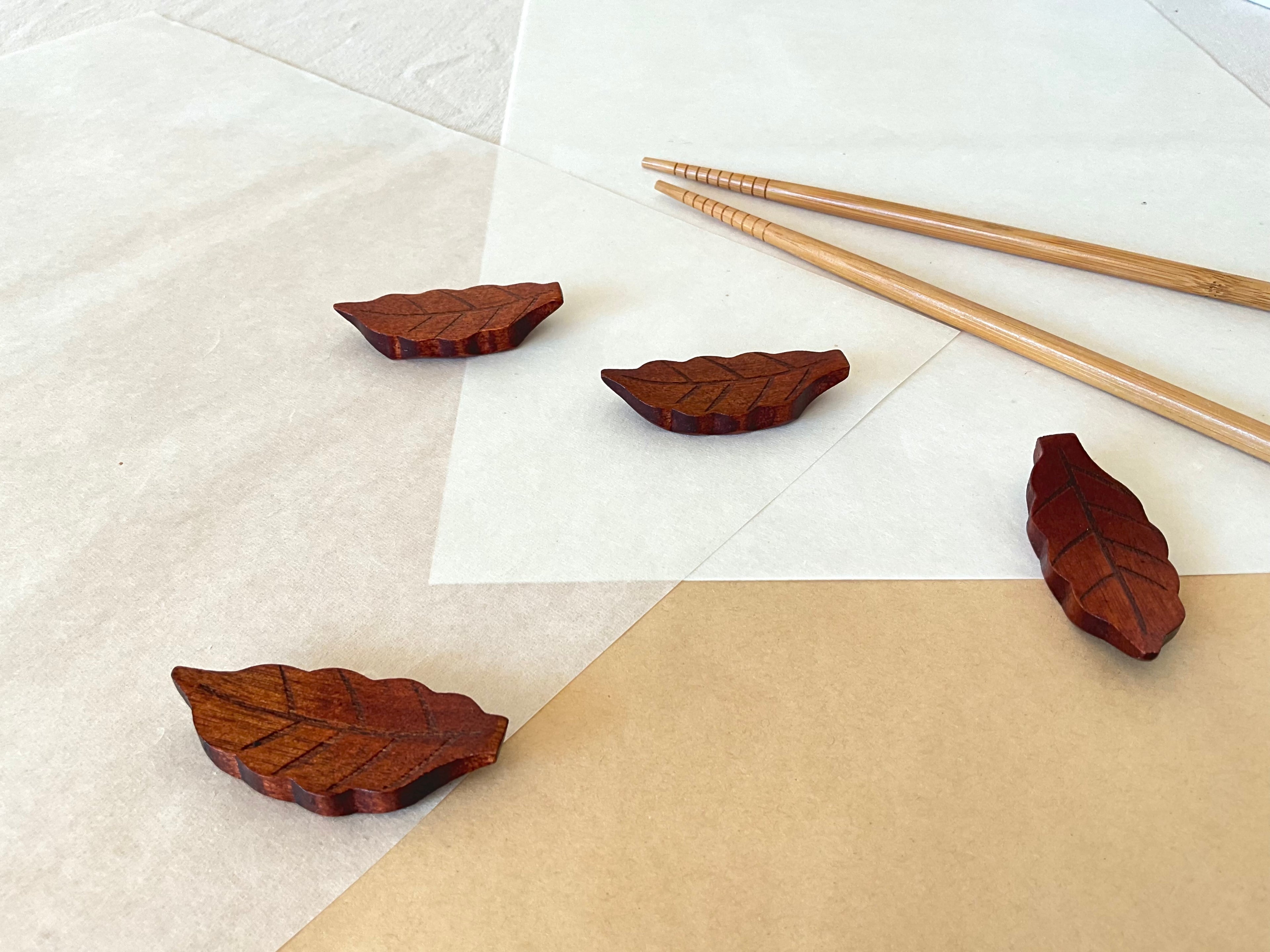 Four wooden leaf chopstick holders scattered on white and kraft paper with bamboo chopsticks in background