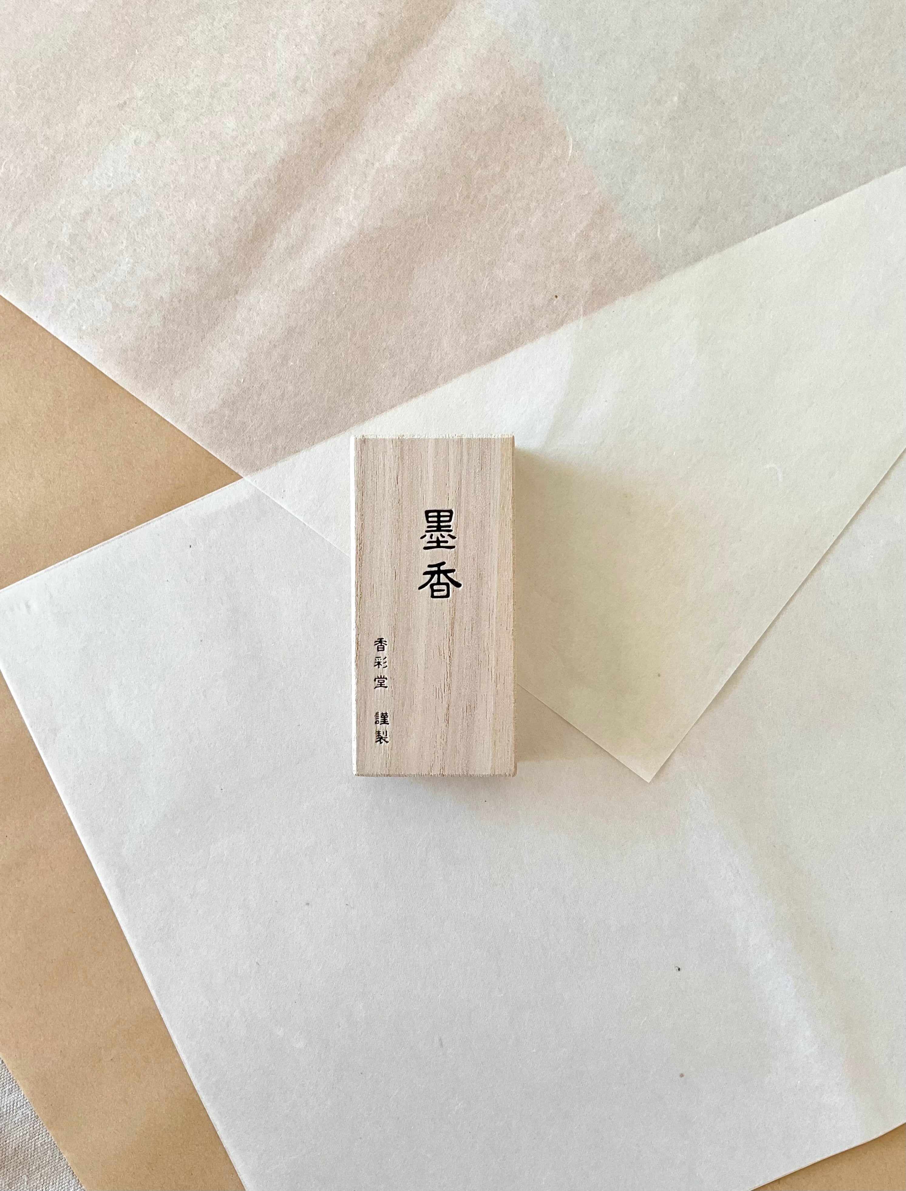 Kousaido Boku-ko Ink Fragrance incense in small paulownia wood box from above on layered washi paper, ink fragrance kanji on natural pale wood grain, Kousaido maker mark below