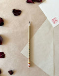 Kobaien fine detail calligraphy brush with sharp pointed tip and bamboo handle printed with Japanese maker markings, resting on layered washi paper with dried rose petals and a red hanko stamp card
