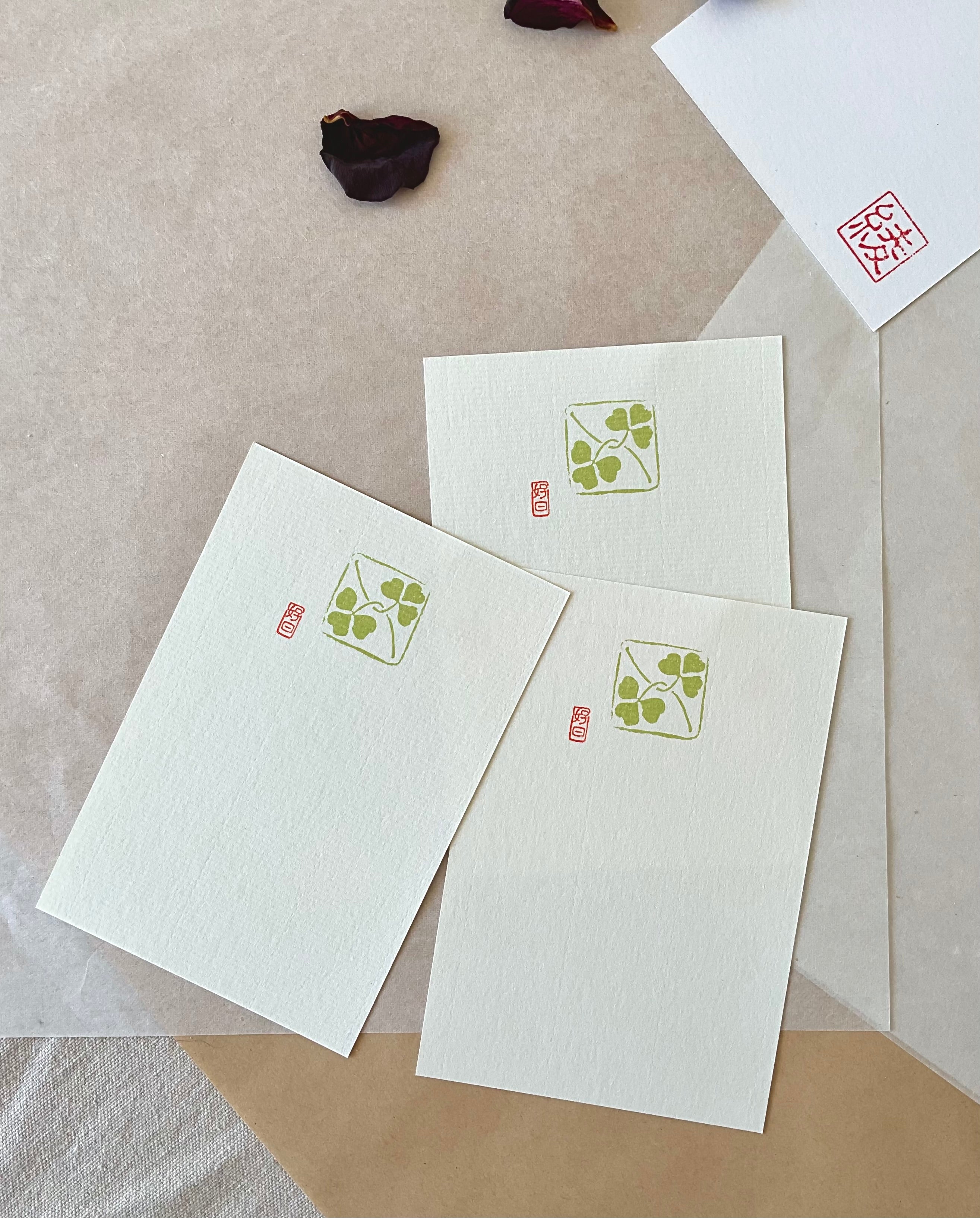Three Genro clover postcards fanned out showing olive green clover illustration on textured paper