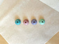 Four round ceramic incense holders in a row on washi paper, glazed in teal, dusty rose, lavender and sage green, each with a small central hole for an incense stick
