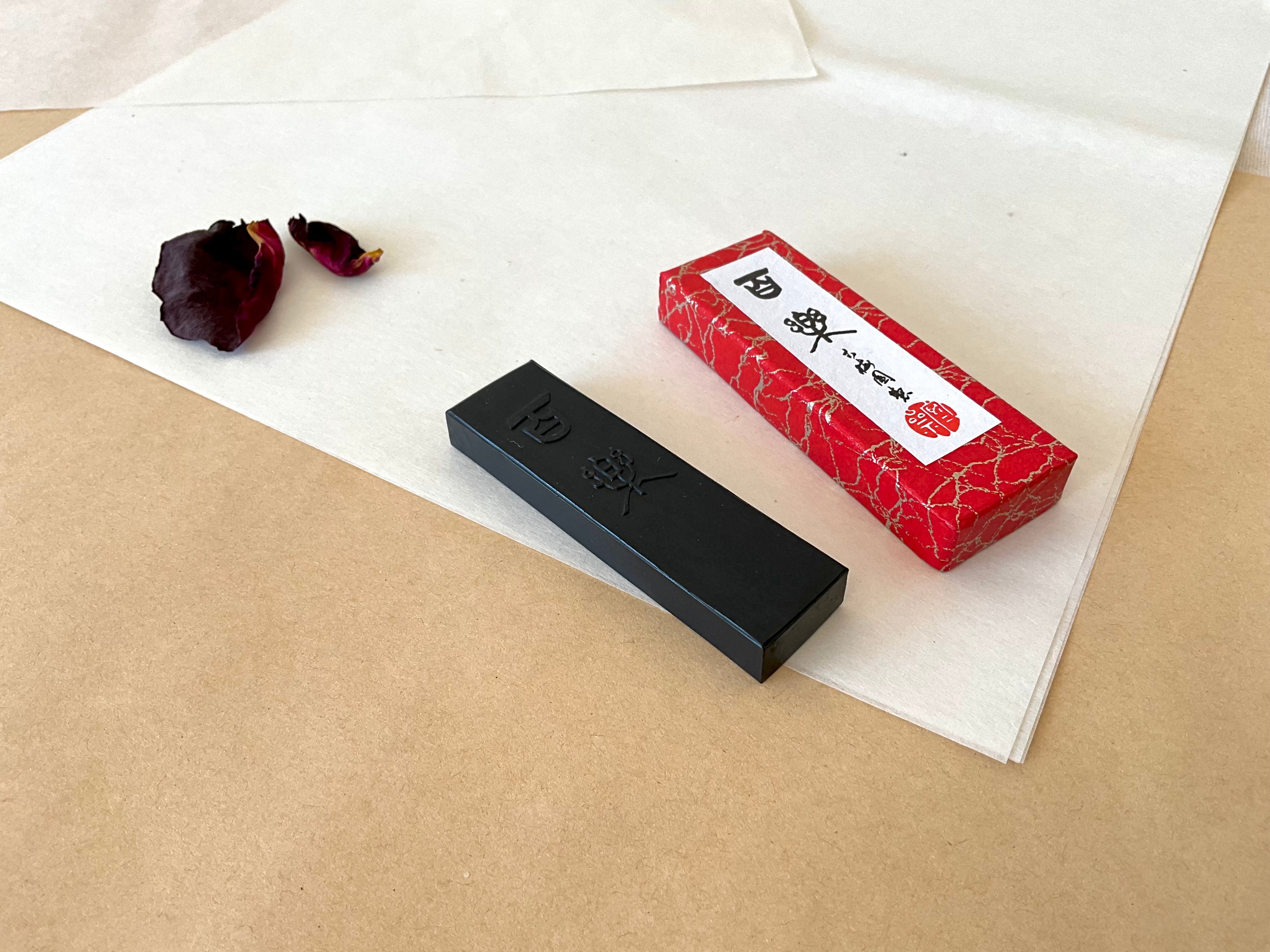 Single Hyoraku black sumi ink stick with engraved characters beside red marbled box on kraft paper