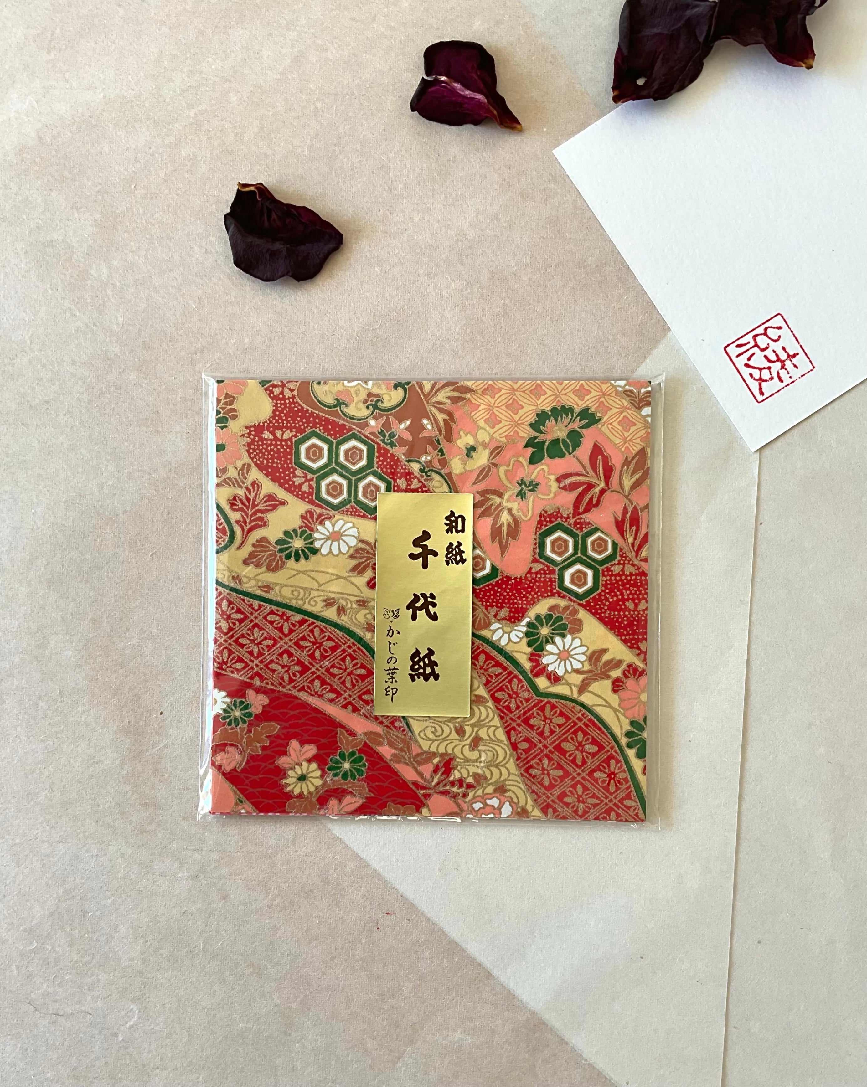 Single sealed pack of Morita Washi chiyogami origami paper with multi-pattern design in deep red, gold and green featuring hexagonal crests and chrysanthemum florals, gold label, with hanko stamp card