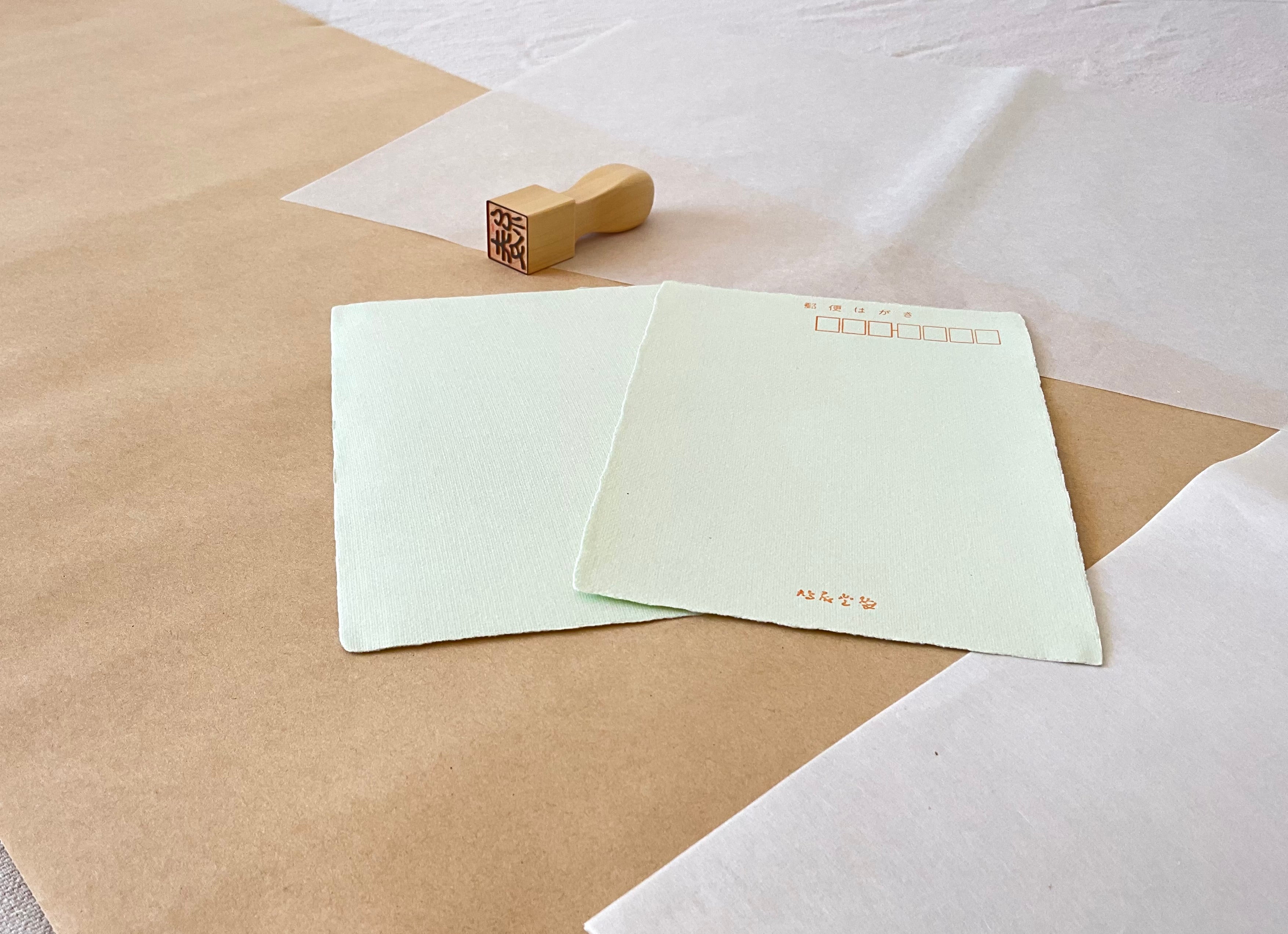 Two green handmade Kyukyodo washi postcards on layered kraft paper with wooden hanko in corner