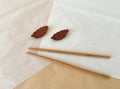 Four wooden leaf chopstick holders scattered on white and kraft paper with bamboo chopsticks in background