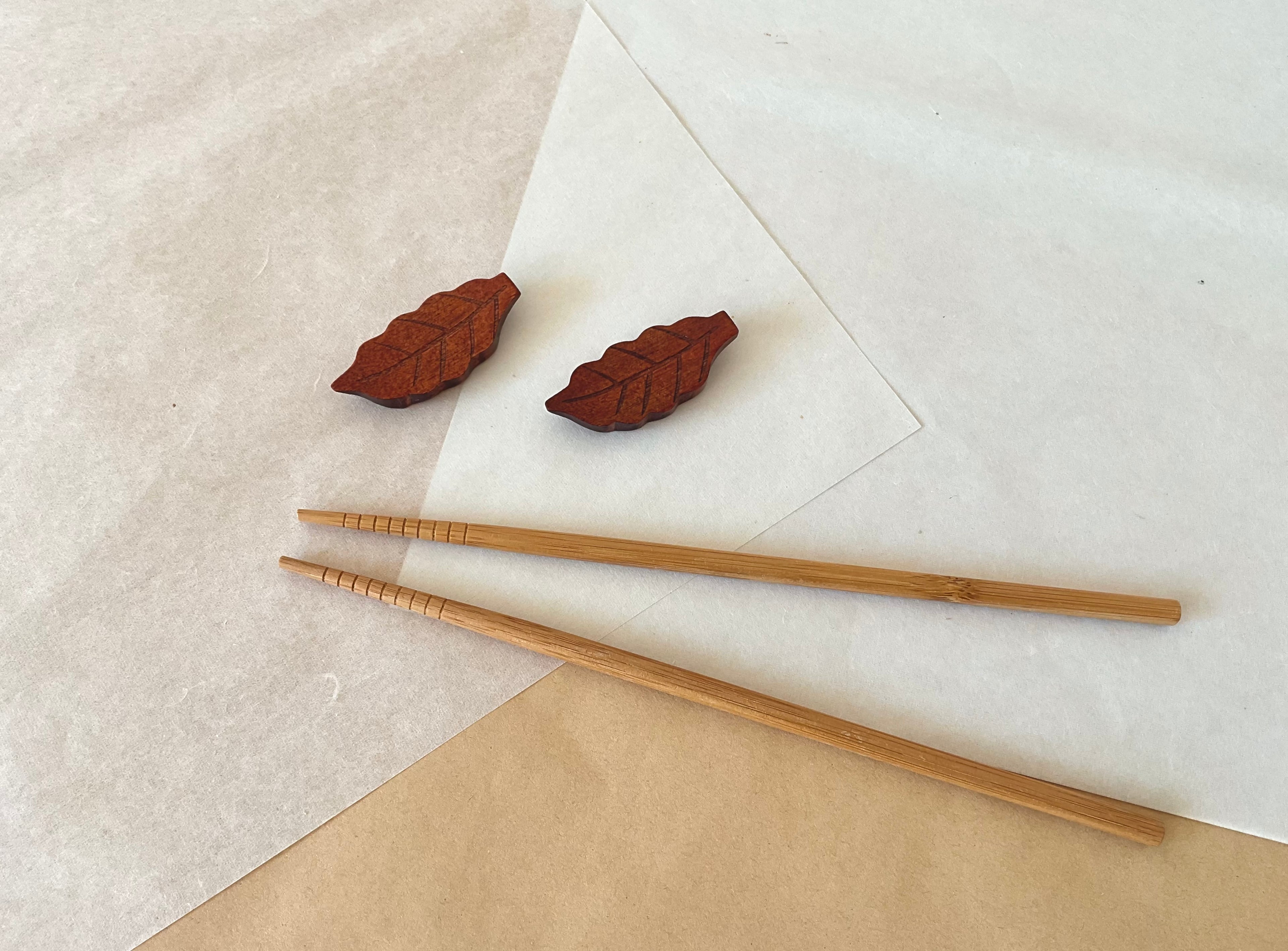 Four wooden leaf chopstick holders scattered on white and kraft paper with bamboo chopsticks in background