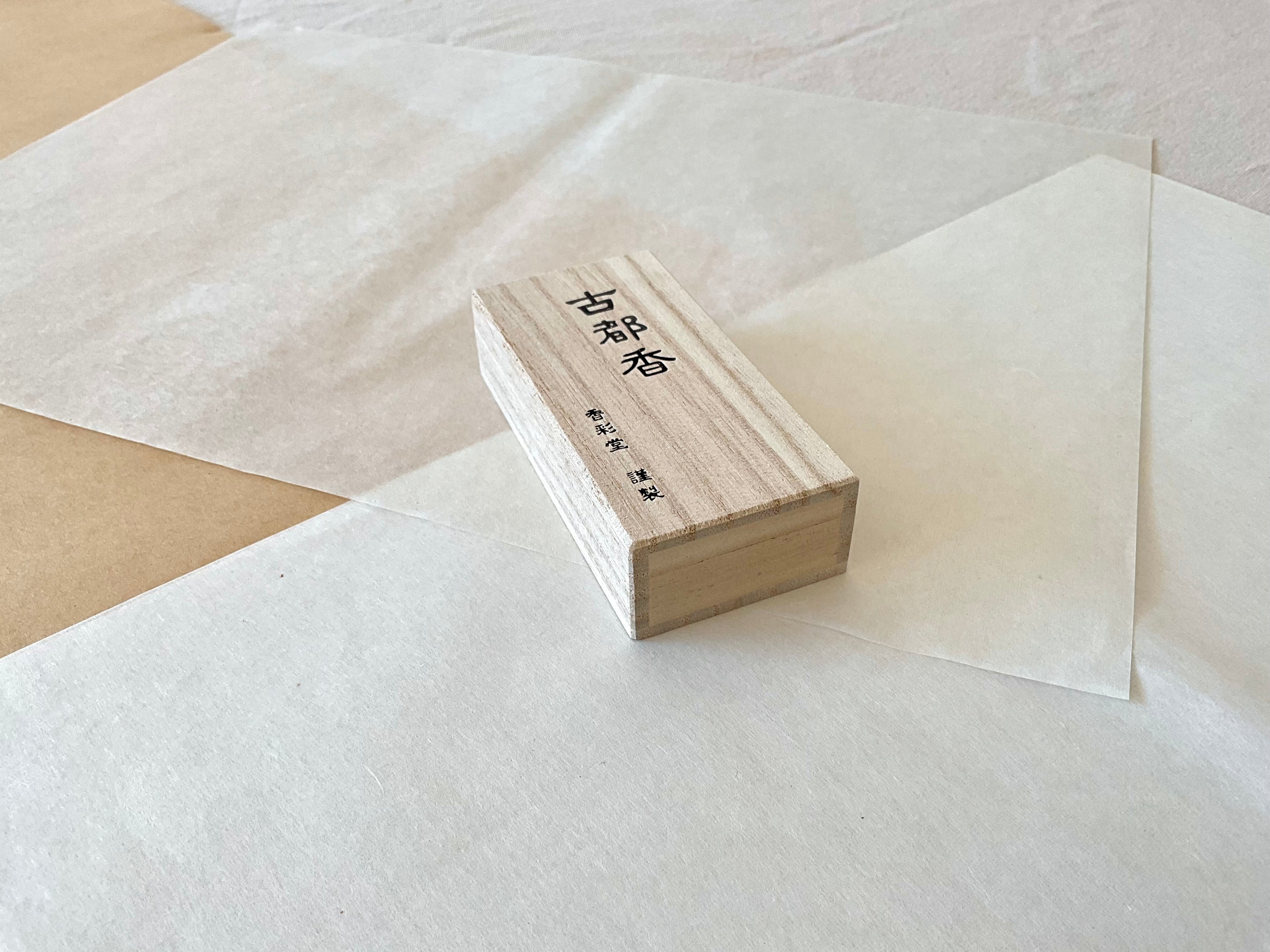 Kousaido Koto-ko Ancient Capital incense paulownia wood box at an angle on layered washi paper, natural wood grain and Japanese kanji visible, minimal clean composition