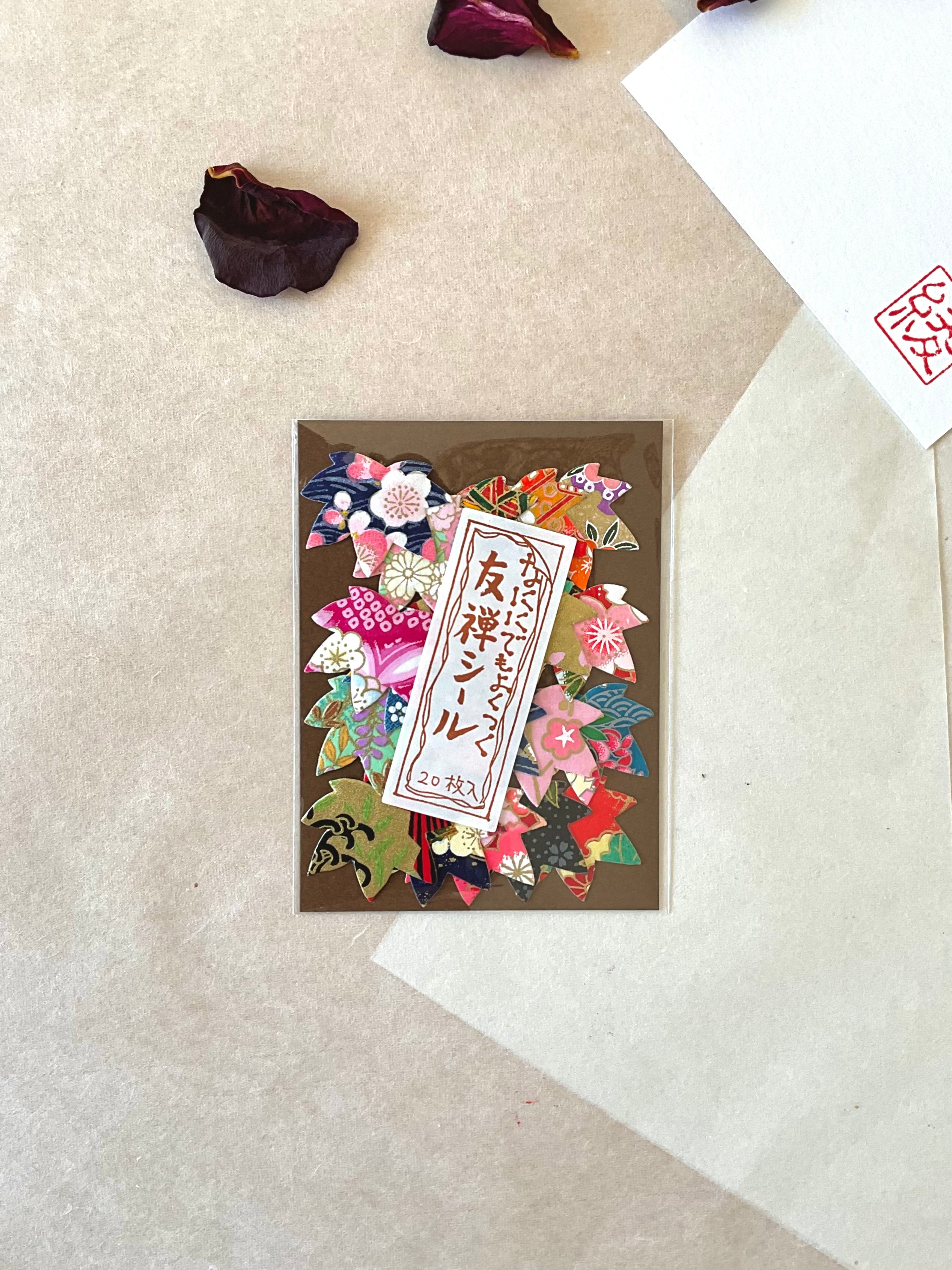 Single pack of Morita Washi yuzen washi stickers flat on neutral washi background, brown card backing covered with 20 mixed flower shaped stickers in traditional Japanese yuzen patterns including navy floral, red sakura, gold and pink chiyogami, with Japanese label and hanko stamp card visible