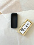 Black polished Japanese suzuri ink stone beside gold presentation box on white washi background