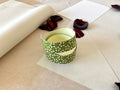 Both sheets of Shogado hand dyed yuzen washi tape laid on top of each other on  washi paper, showing Olive green with white daisy and red center floral print repeated across both strips, dried rose petals nearby