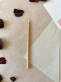 Kobaien fine detail calligraphy brush with sharp pointed tip and bamboo handle, resting on layered washi paper with dried rose petals and a red hanko stamp card