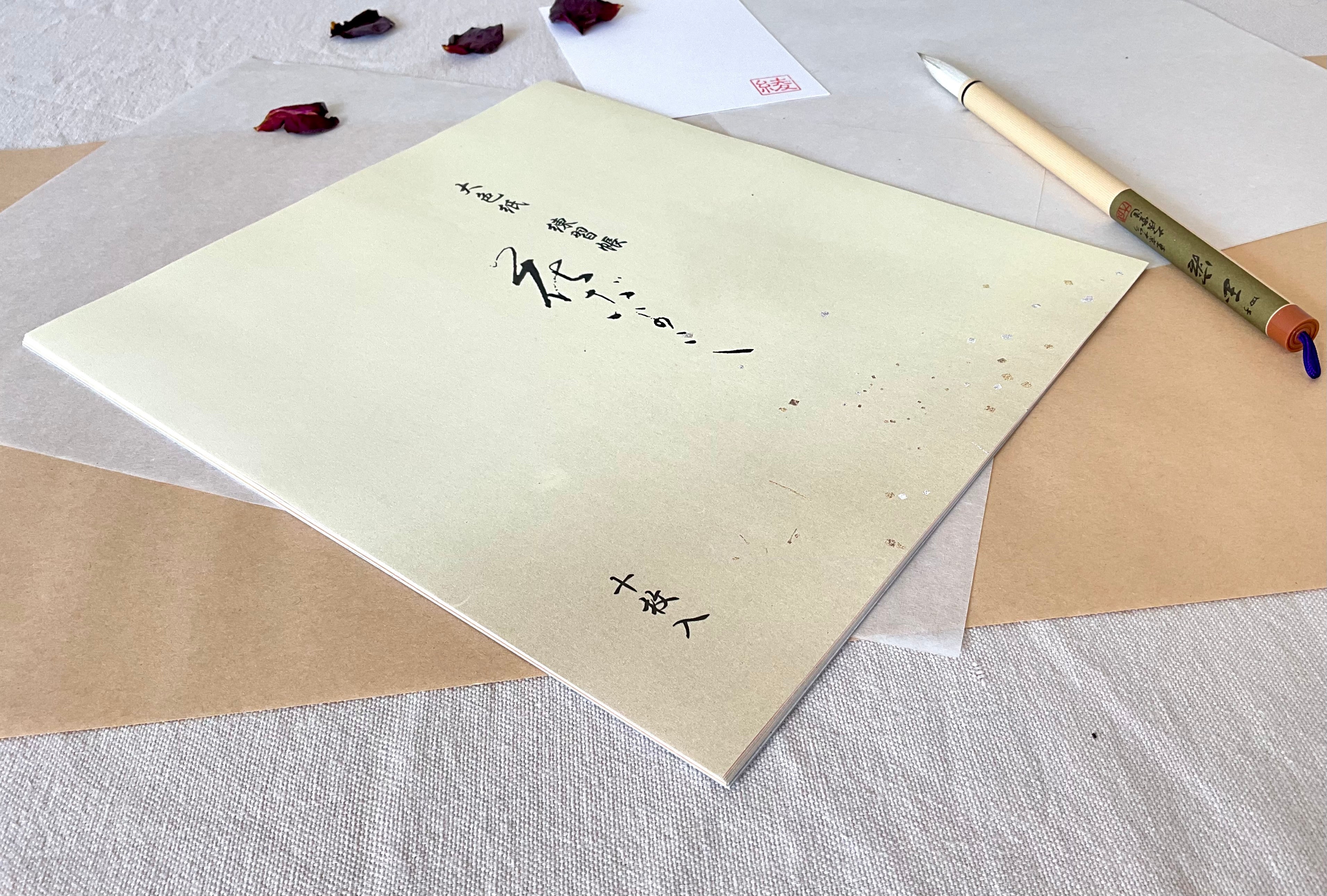Kyokuodo shikishi paper sleeve placed at an angle beside a Japanese calligraphy brush, on layered washi and linen, with a hanko stamp card in the background