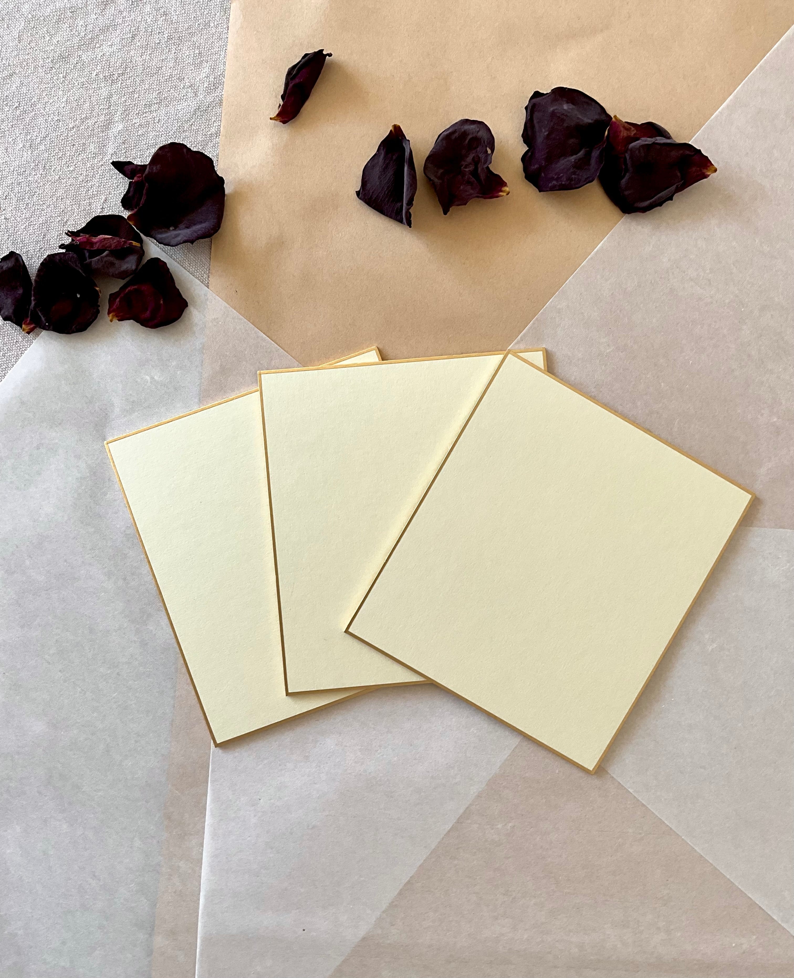 Three large cream Kyukyodo shikishi boards fanned out at an above view on layered washi and kraft paper with dried dark rose petals to the top
