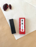 Hyoraku black ink stick beside red marbled Kobaien presentation box on layered washi paper