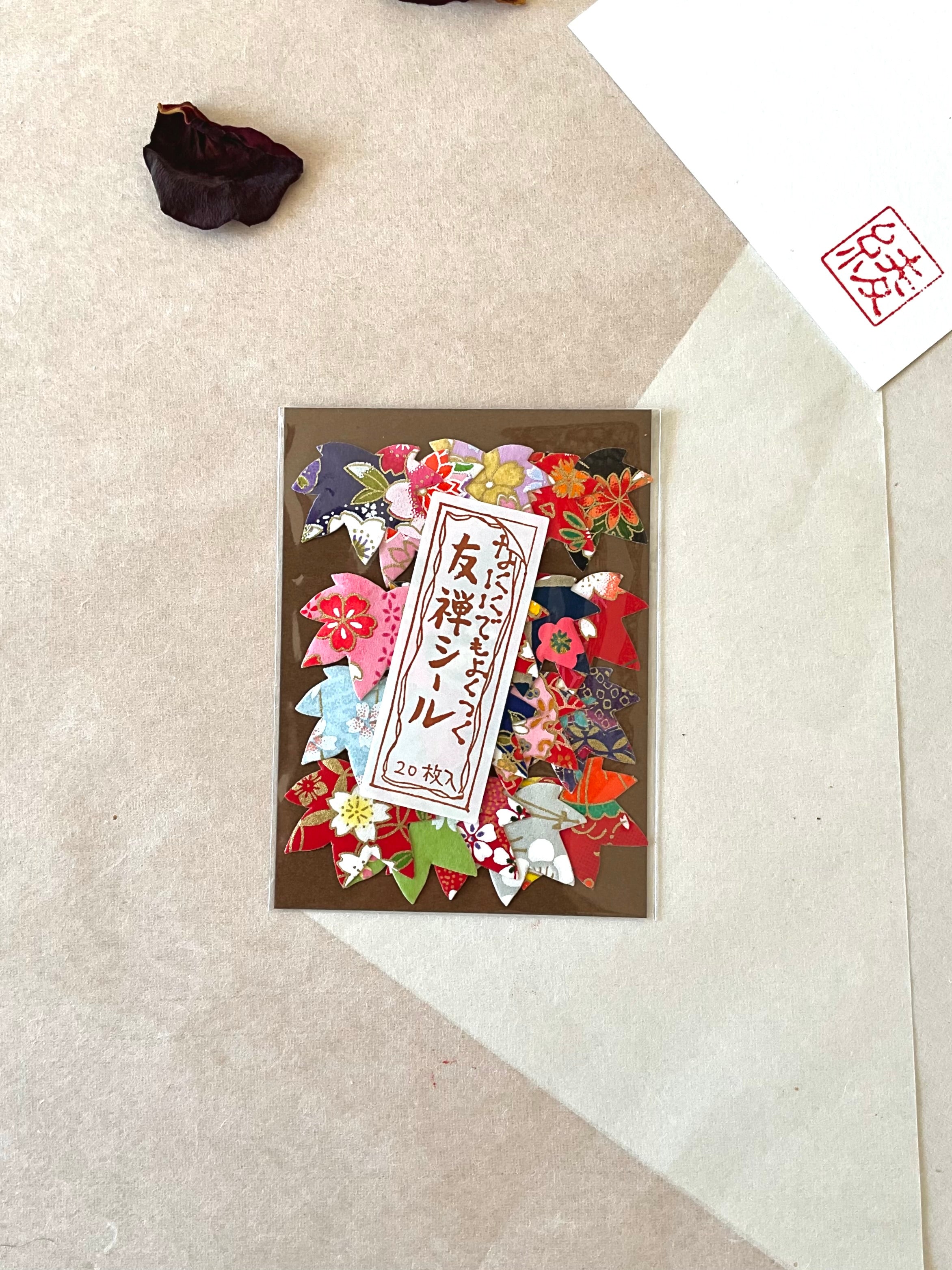 Single pack of Morita Washi yuzen washi stickers on neutral background, showing flower shaped sticker assortment with purple, red, pink, blue and gold chiyogami patterns, Japanese label reading yuzen shiru 20 pieces, with hanko stamp card