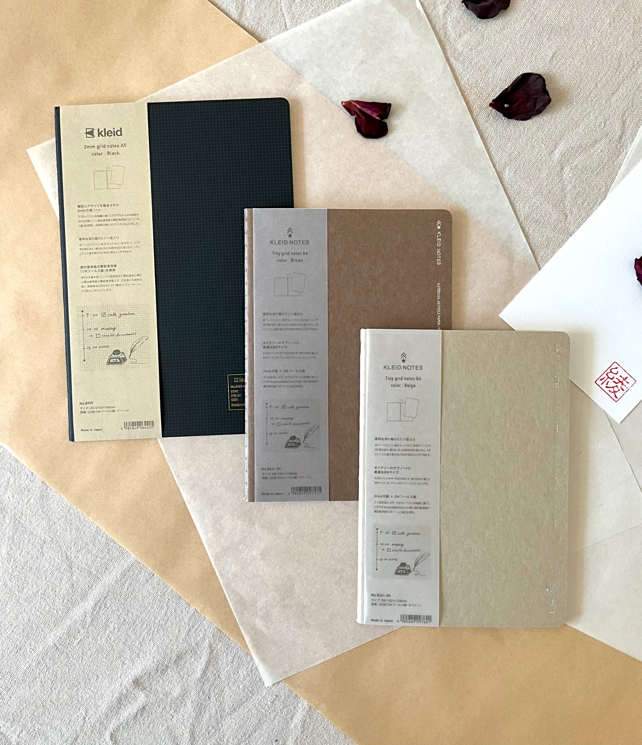 Three Kleid notebooks fanned out showing black A5 and two B6 covers on layered washi and kraft paper