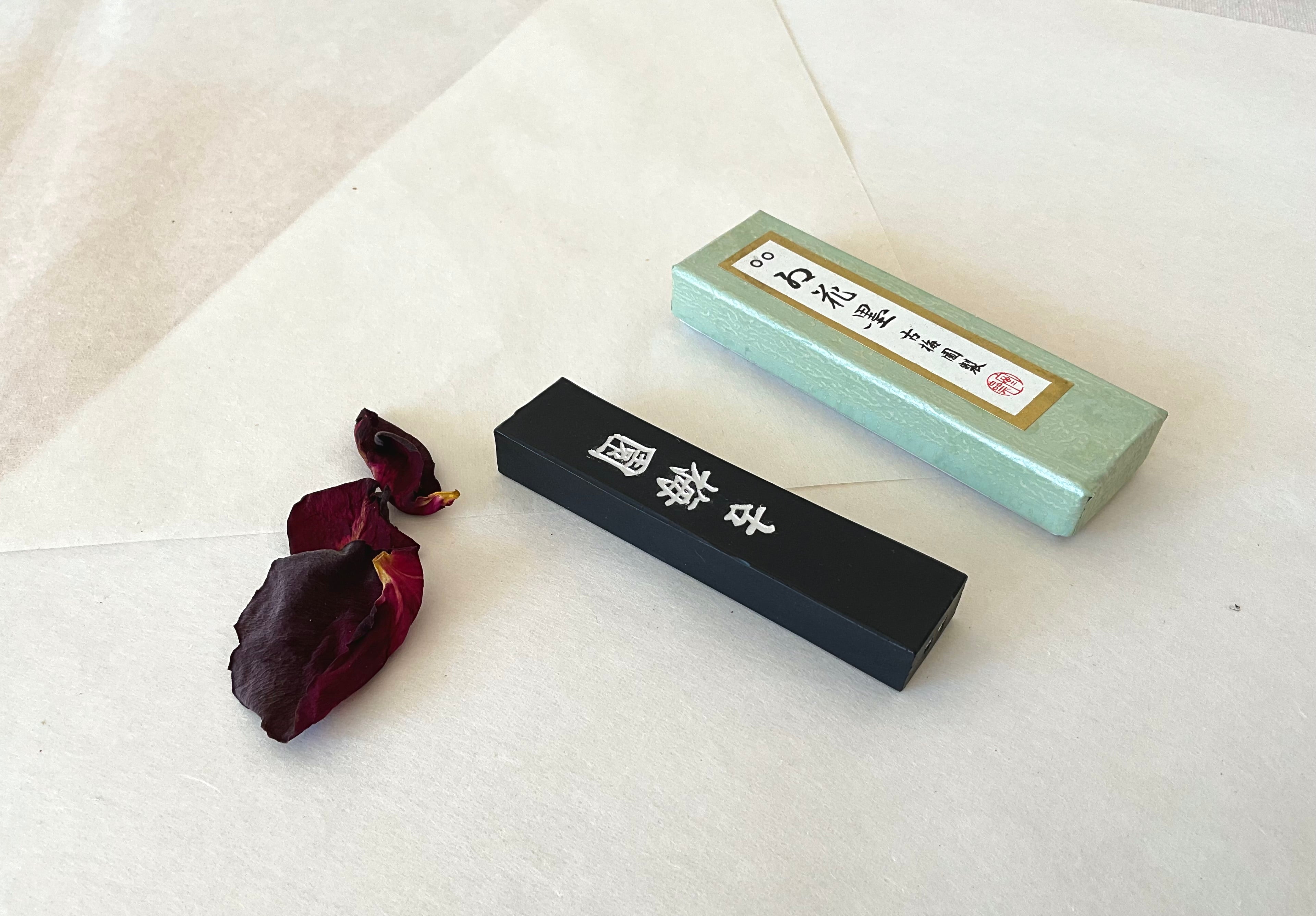 Kokaun black ink stick beside mint green Kobaien presentation box on white washi paper background
