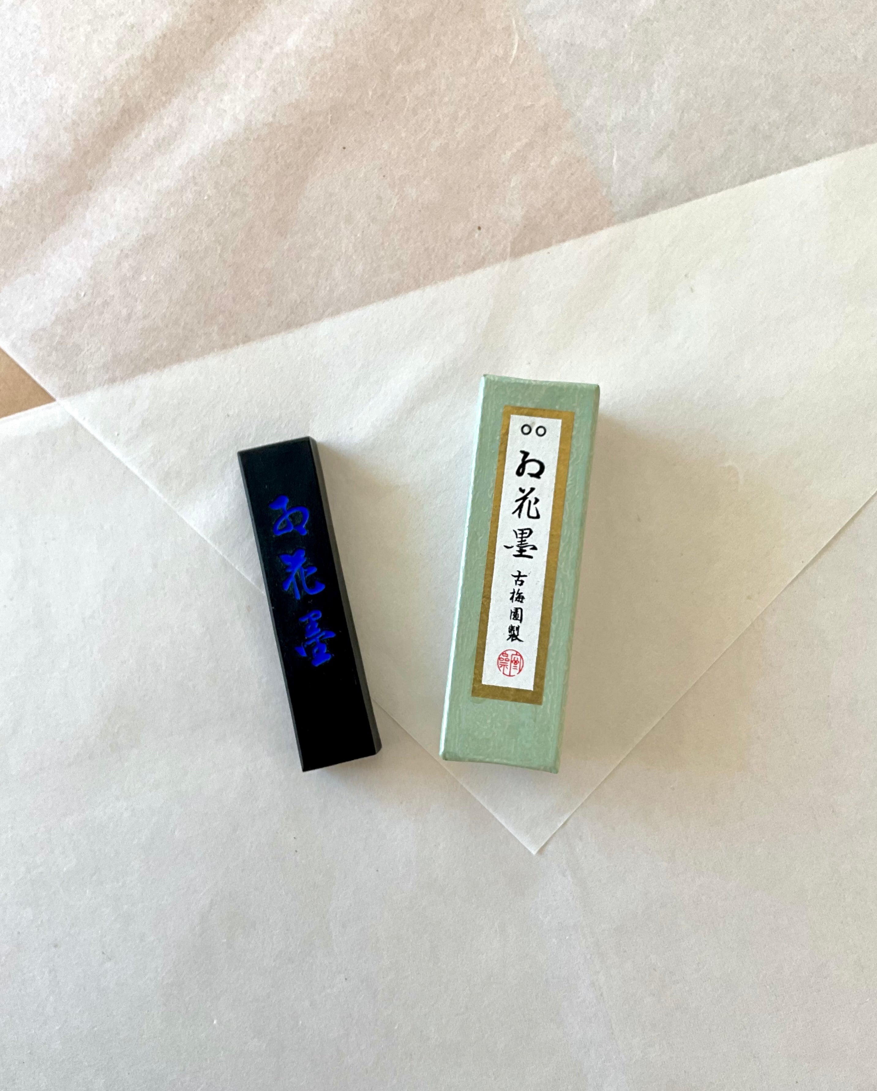Kokaun ink stick with blue iridescent lettering beside green box by Kobaien on layered washi paper