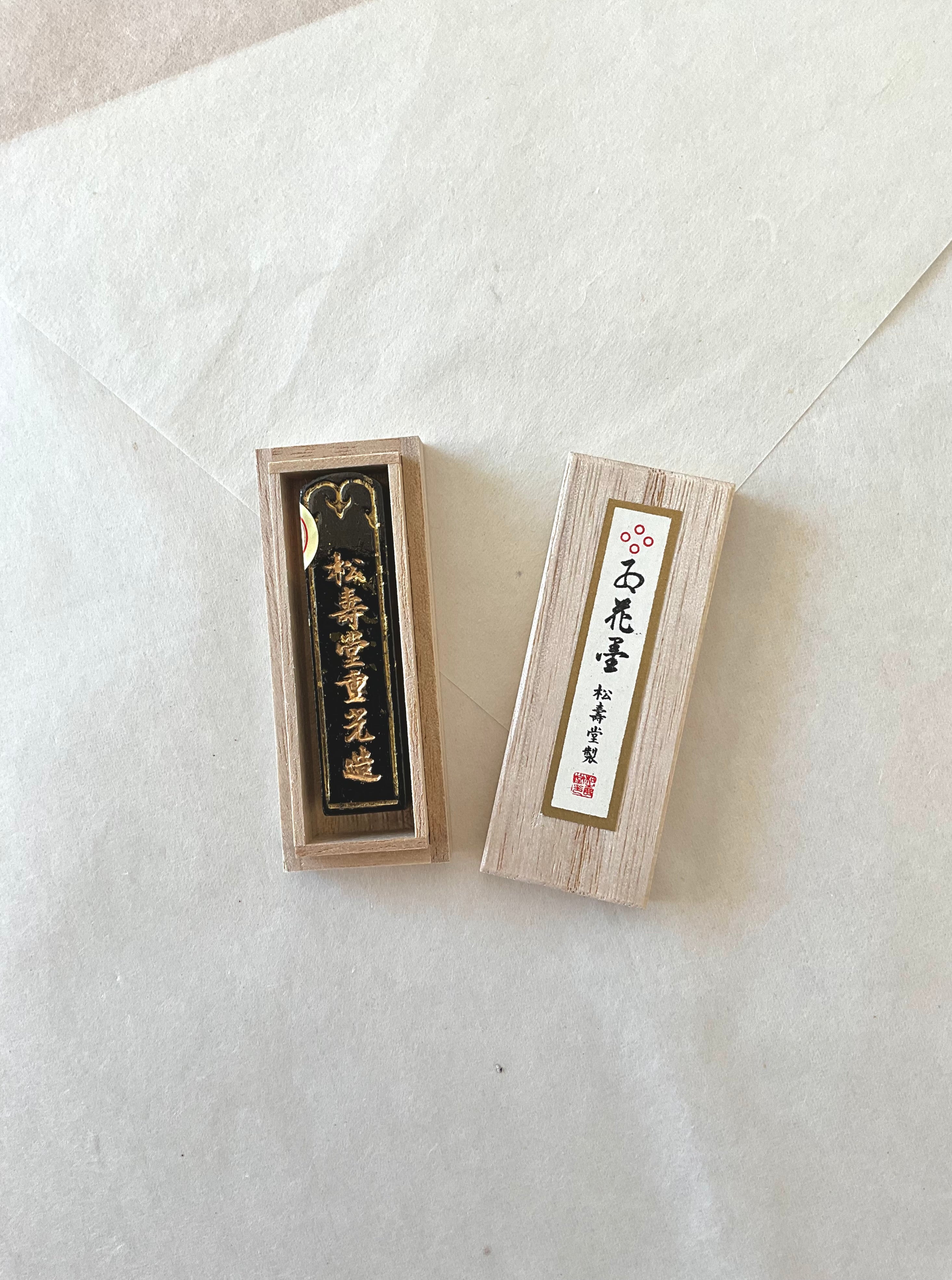 Gokaun premium black ink stick with gold lettering beside pale wooden presentation box on washi paper