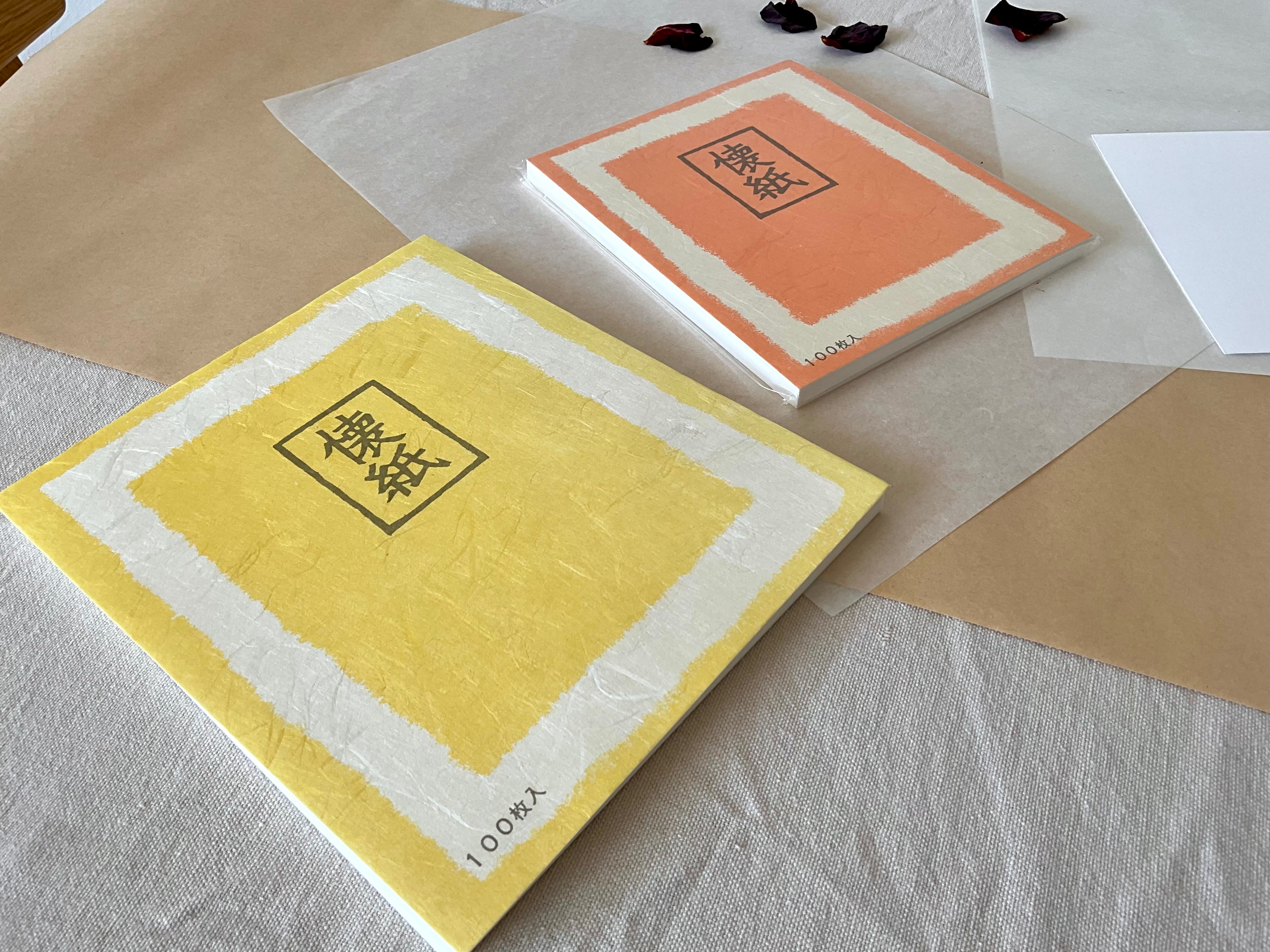 Two Morita Washi kaishi paper packs side by side on linen and washi paper, one in yellow and one in terracotta orange, both with 100 sheet count and kaishi kanji label, showing the two available sizes