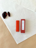 Vermillion red ink stick beside its red presentation box with Japanese calligraphy label on washi paper
