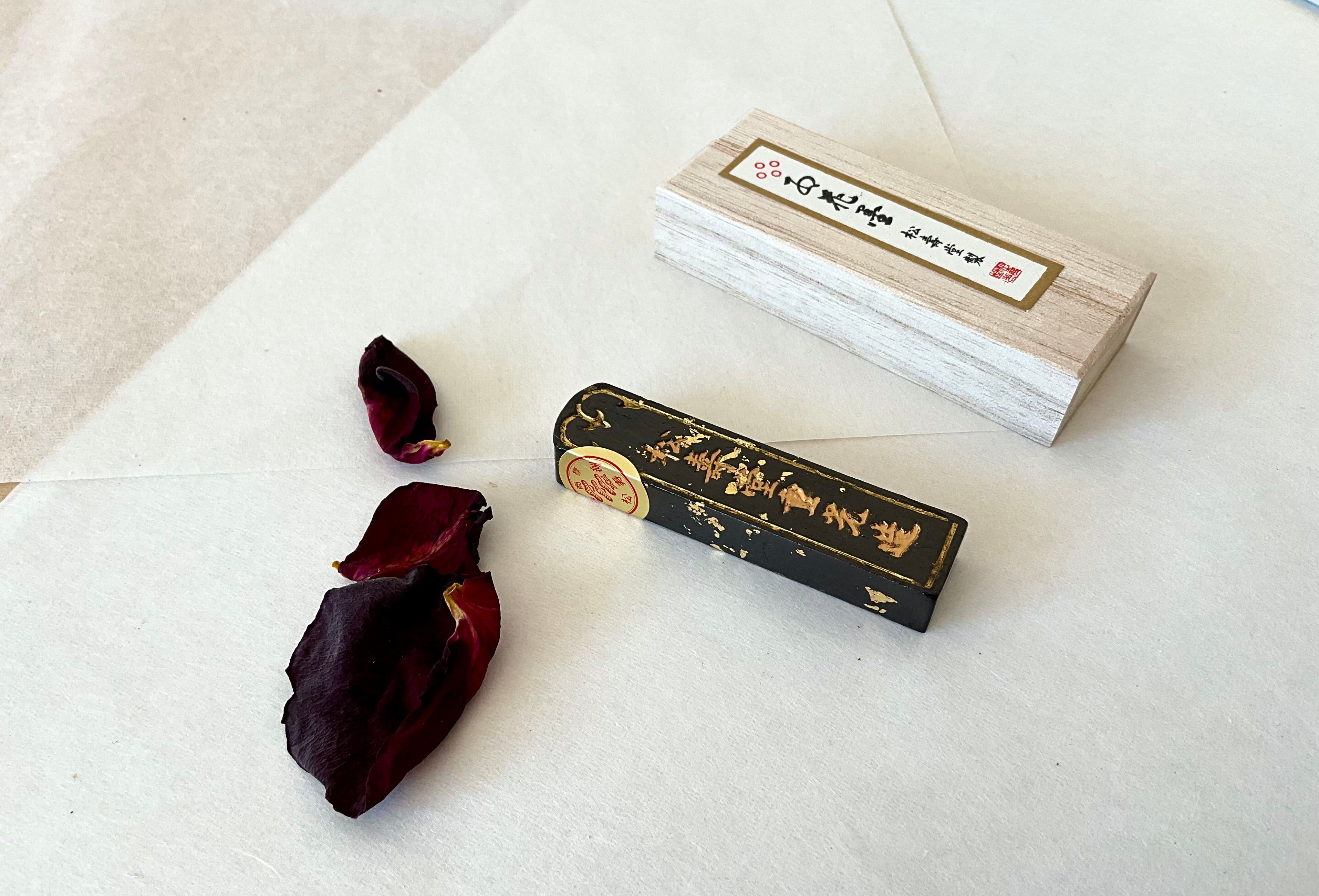 Gokaun ink stick removed from wooden box showing gold calligraphy detail on lacquered black surface