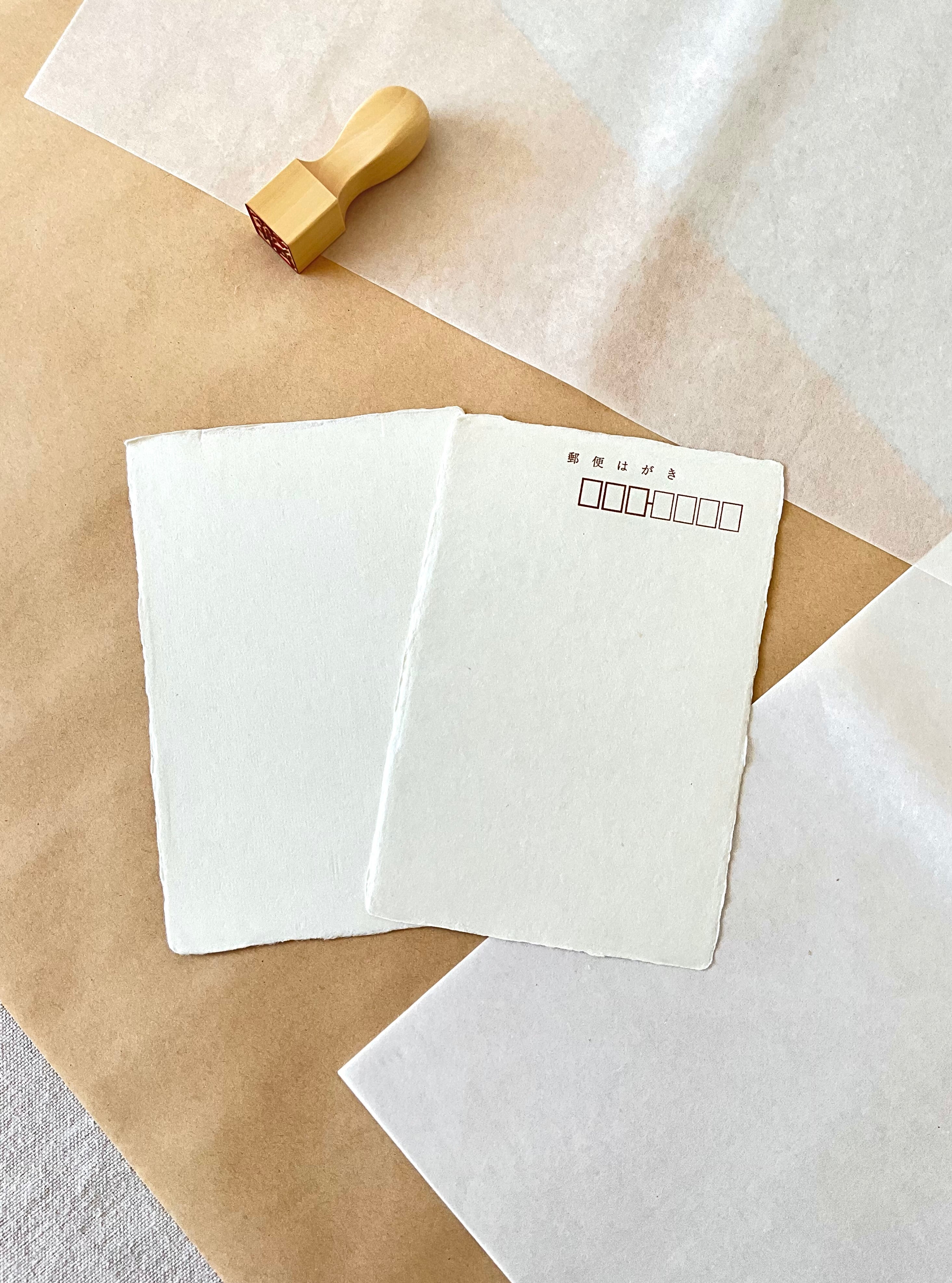 Two cream handmade Kyukyodo postcards on layered paper background with wooden hanko stamp