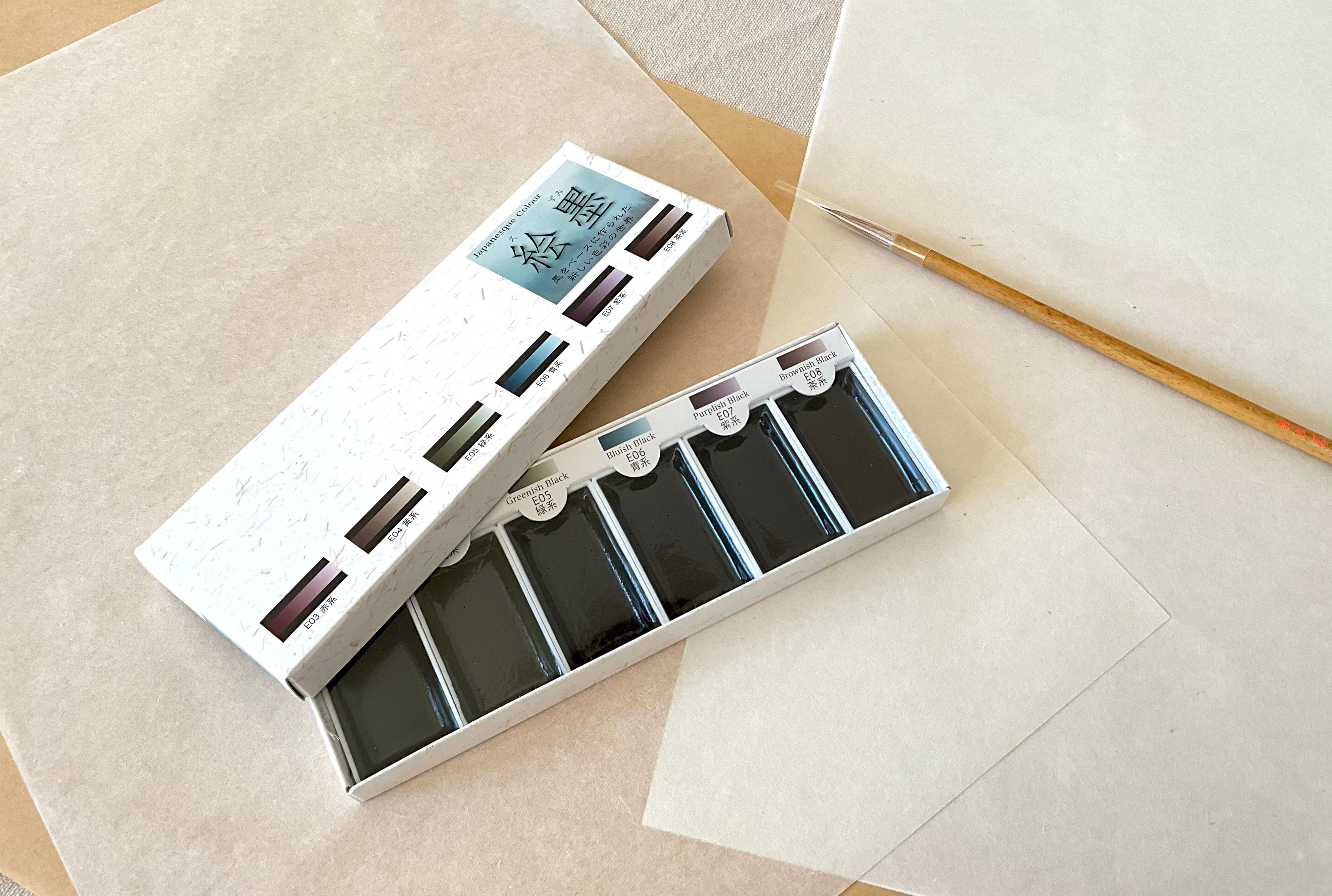 Ezumi Classic set open showing six dark sumi ink watercolor pans with calligraphy brush on washi paper