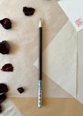 Saiundo calligraphy brush with dark lacquered handle and printed paper label, full pointed bristle, resting on layered washi paper with dried rose petals and a red hanko stamp card