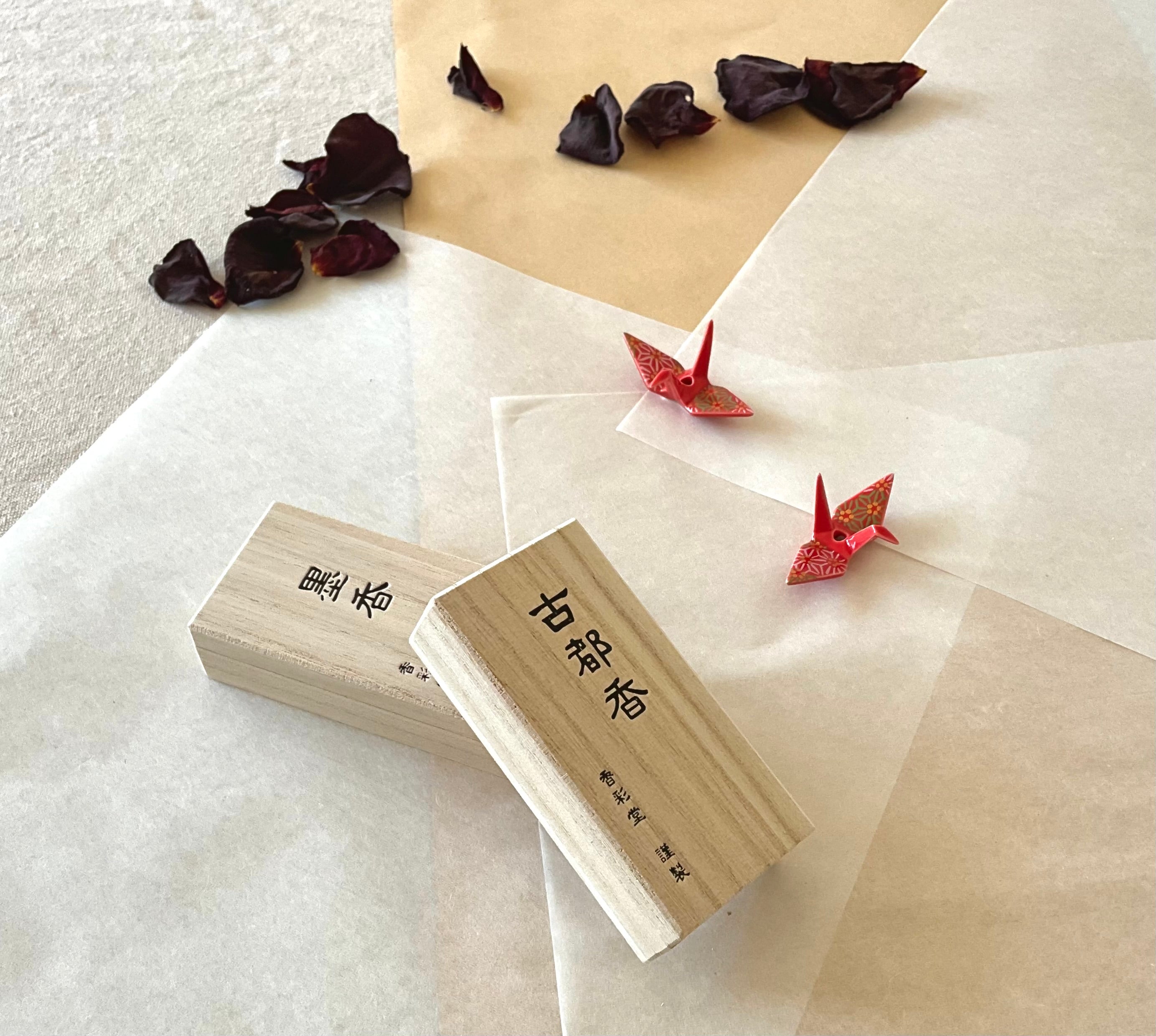 Two boxes one over the other with two red origami cranes on layered washi and kraft paper and washi paper, scattered dried rose petals