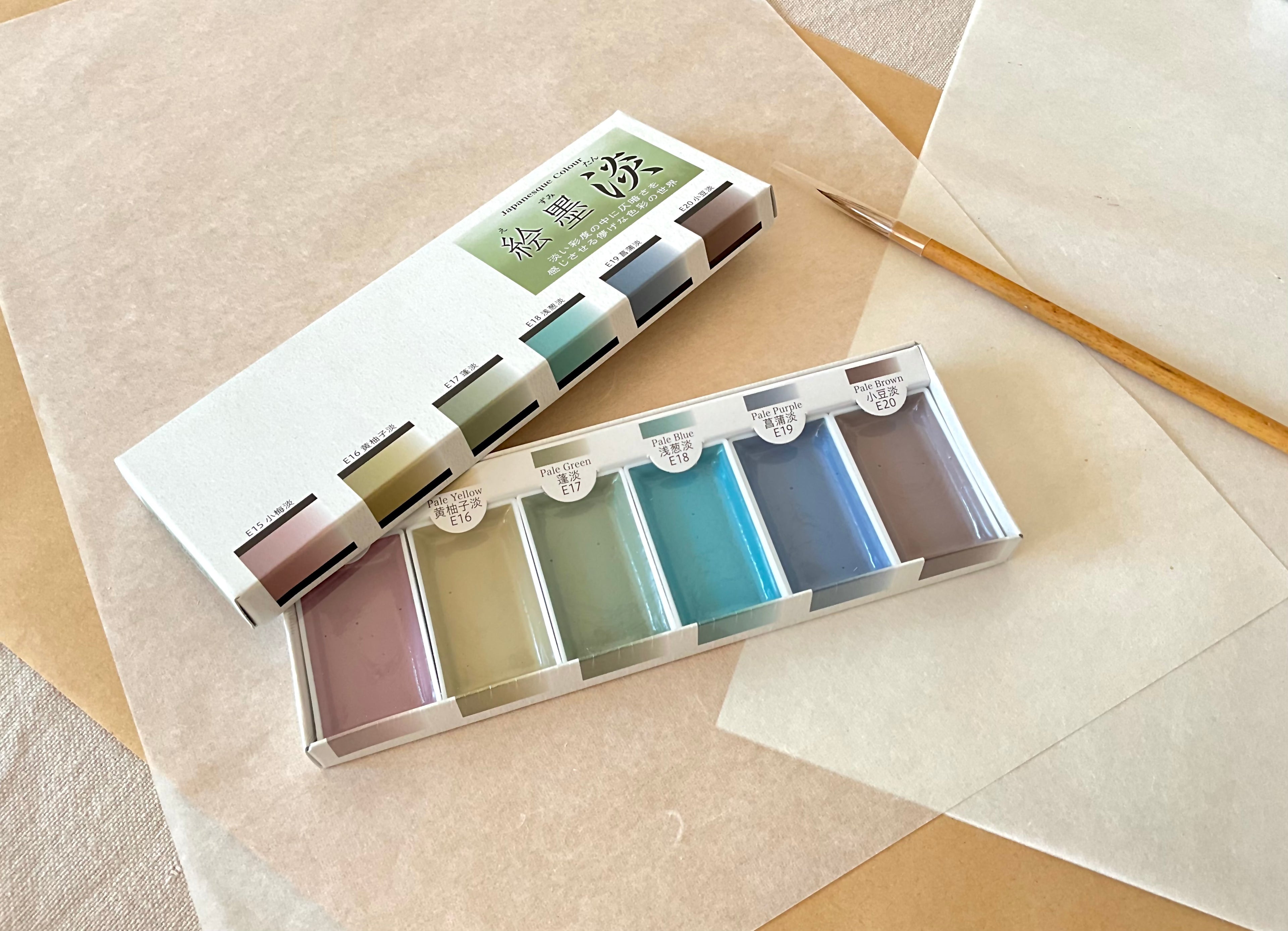 Ezumi Tan set open showing six pale sumi watercolor pans with calligraphy brush beside it