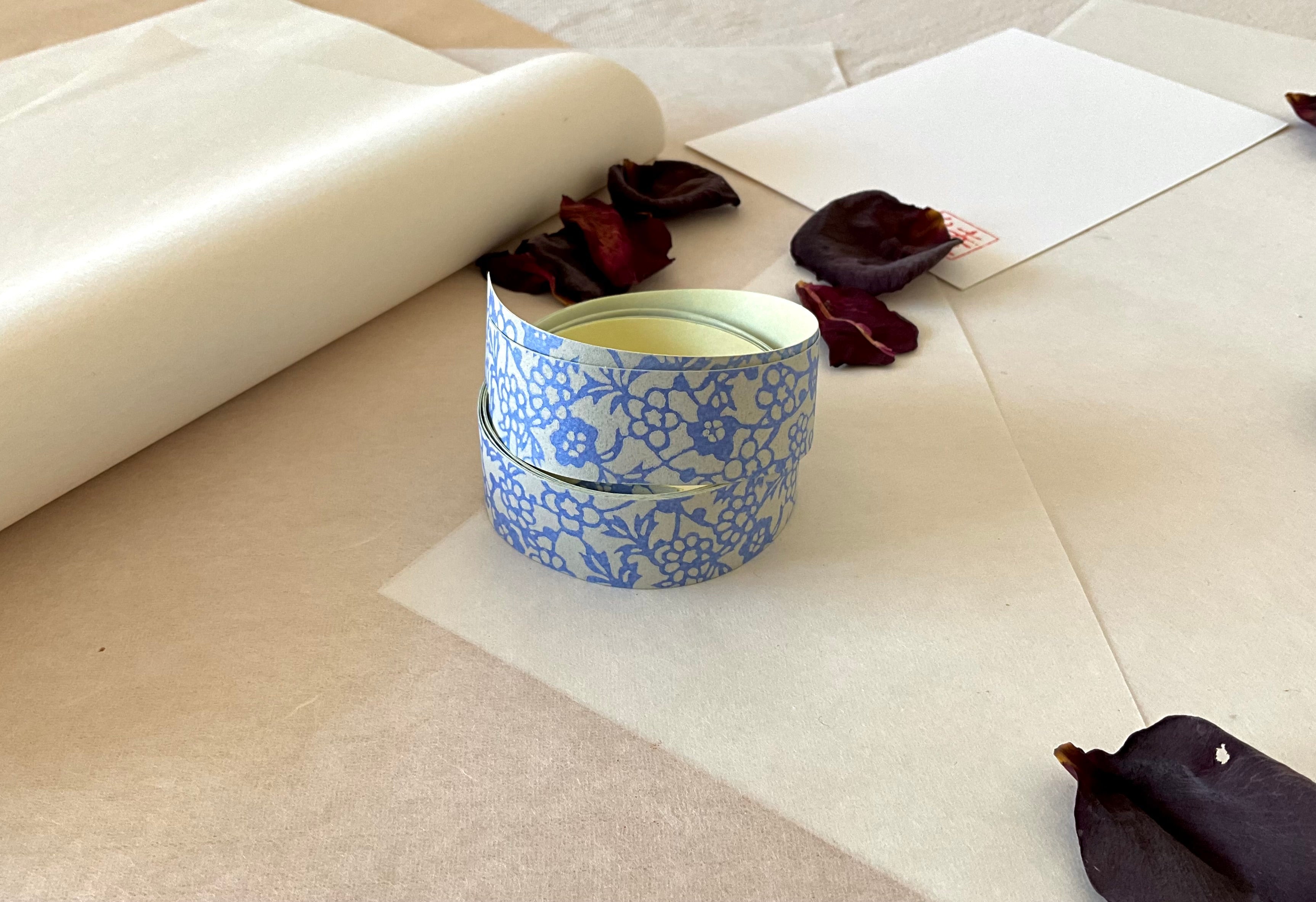 Both sheets of Shogado hand dyed yuzen washi tape laid side by side on washi paper, showing Grey-blue with blue floral block print pattern repeated across both strips, dried rose petals nearby