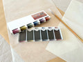 Ezumi Mei set open showing six shadow color watercolor pans with calligraphy brush on washi paper